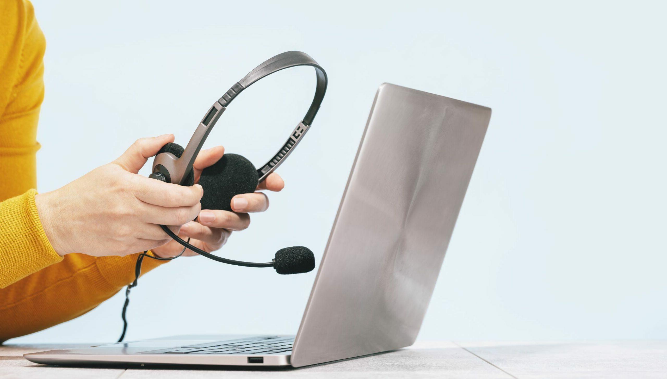 Online-DSH-Training: Eine Person sitzt vor einem Laptop und hält ein Headset in der Hand.