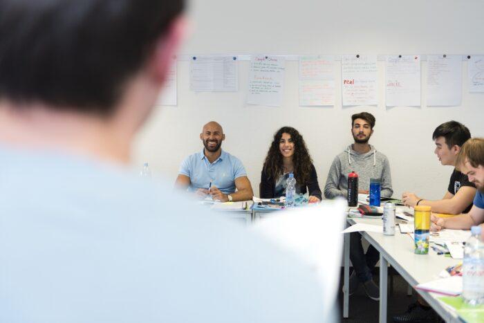 Gruppenprogramme: Ein Lehrer unterrichtet eine Gruppe von begeisterten Studierenden in einem hellen Klassenraum.