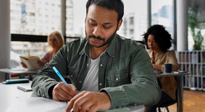 telc Deutsch B1-B2 Pflege: A young nurse sits in a classroom and writes a German exam.