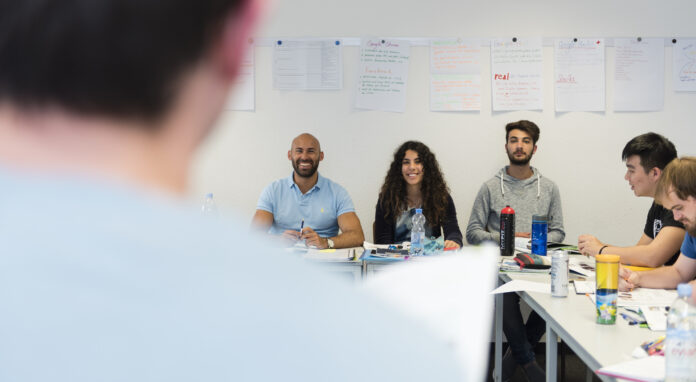 Group programmes: A lecturer teaches a group of delighted students in a sunlit classroom.