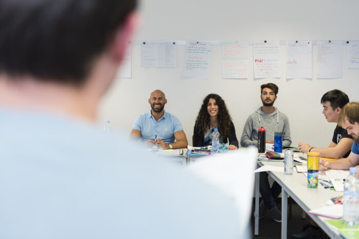 Group programmes: A lecturer teaches a group of delighted students in a sunlit classroom.